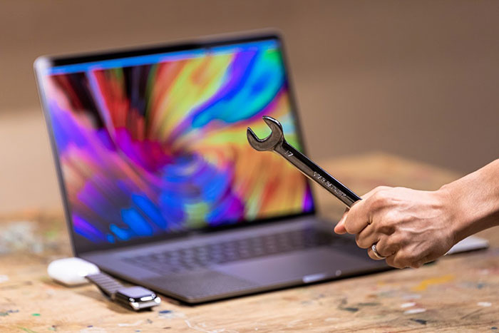 Man holding up wrench in front of laptop